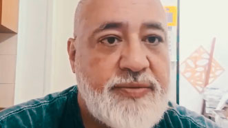 Airan veste camiseta verde e dá seu depoimento sobre hipnoterapia para síndrome do pânico e depressão. Ele tem barba