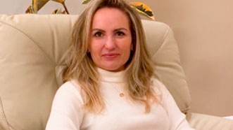 Dani Verdugo está sentada em uma poltrona. Ela usa um pullover bege e tem cabelos loiros compridos. Ela faz seu depoimento sobre sua hipnoterapia para burnout, esgotamento e falta de foco.