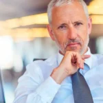 Homem de camisa azul clara e gravata azul escura, está com a mão no queixo representando resistência em relação a liderança situacional