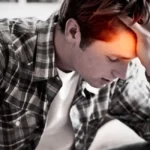 Homem está com a mão esquerda apoida na cabeça. A imagem é em preto e branco, mas a testa dele está iluminada em tons de laranja e vermelho, representando a dor social e dor física