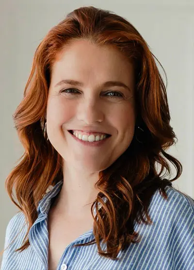 Foto de Alessandra Palazzin. Ela é ruiva, tem cabelo um pouco abaixo do ombro e veste uma camisa azul clara