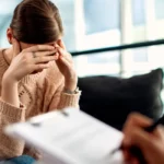 Uma mulher está em uma sessão de hipnoterapia e está com as mãos na testa, demonstrando esgotamento mental
