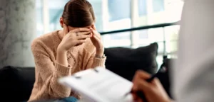 Uma mulher está em uma sessão de hipnoterapia e está com as mãos na testa, demonstrando esgotamento mental