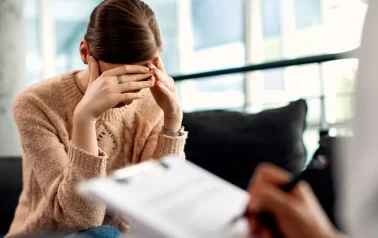 Uma mulher está em uma sessão de hipnoterapia e está com as mãos na testa, demonstrando esgotamento mental